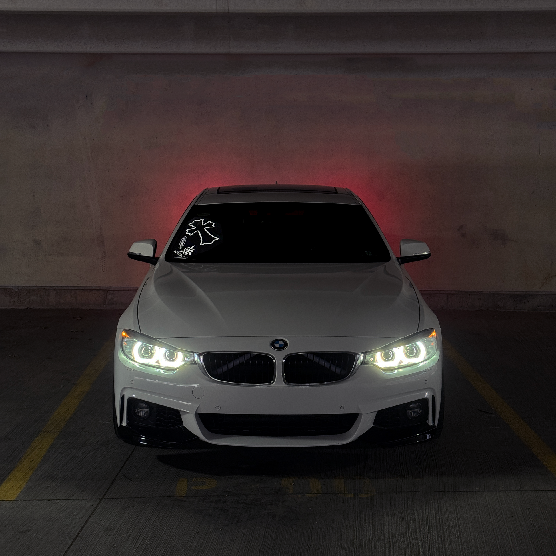 White BMW car with illuminated headlights in a dark parking garage.